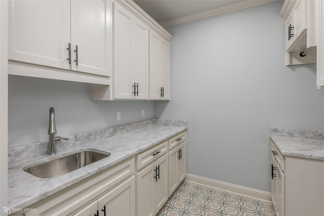 kitchen featuring light tile patterned floors, baseboards, light stone countertops, white cabinetry, and a sink