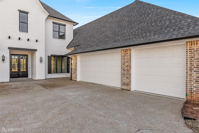 exterior space featuring driveway, brick siding, roof with shingles, and french doors