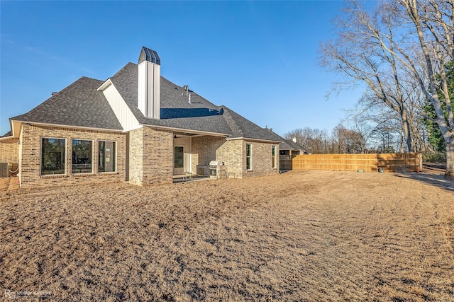 back of house featuring a chimney, brick siding, a fenced backyard, and roof with shingles