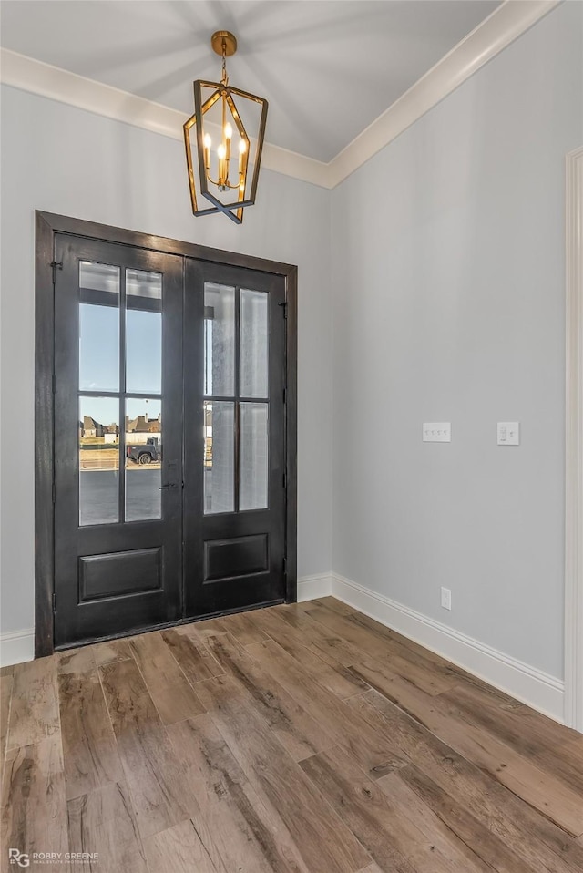 foyer with french doors, a notable chandelier, ornamental molding, wood finished floors, and baseboards