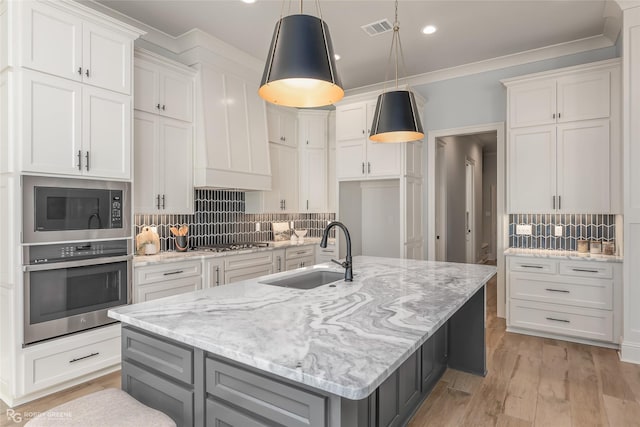 kitchen with a kitchen island with sink, a sink, visible vents, white cabinets, and appliances with stainless steel finishes