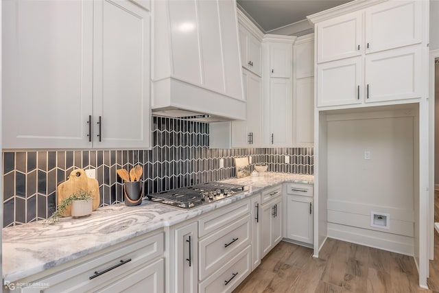 kitchen featuring tasteful backsplash, stainless steel gas stovetop, light wood-style floors, white cabinets, and light stone countertops