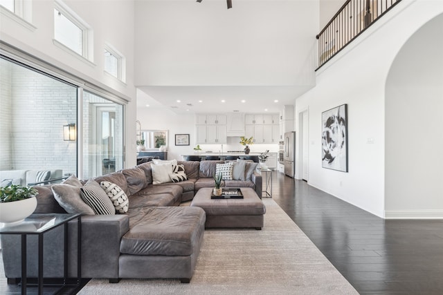 living area with arched walkways, dark wood-style flooring, baseboards, and a high ceiling