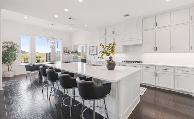 kitchen with a center island with sink, light countertops, custom range hood, white cabinets, and a sink