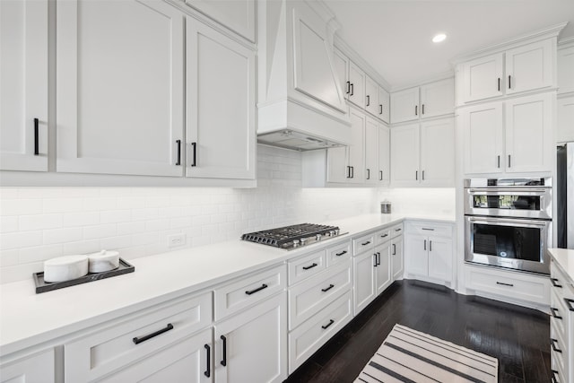 kitchen with tasteful backsplash, dark hardwood / wood-style floors, premium range hood, white cabinetry, and appliances with stainless steel finishes