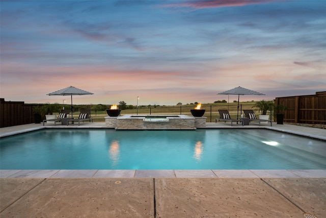 pool at dusk featuring a patio area and an in ground hot tub