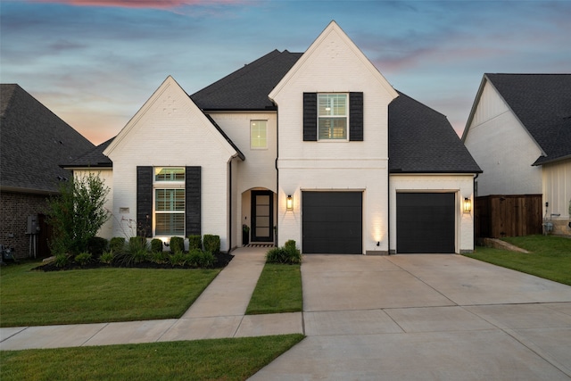 view of front of property featuring brick siding, a yard, a shingled roof, concrete driveway, and fence