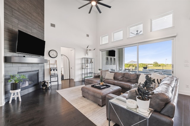 living room featuring ceiling fan, dark wood-type flooring, a tile fireplace, and a towering ceiling