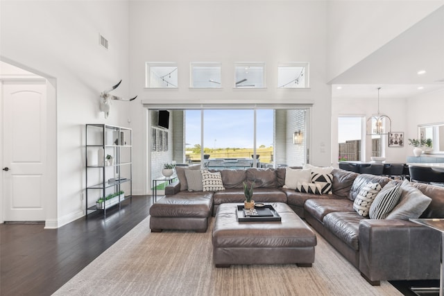 living room with dark wood-type flooring, visible vents, a high ceiling, and an inviting chandelier