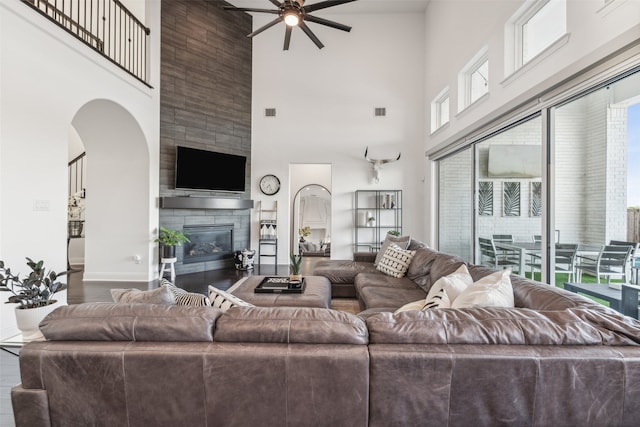 living room featuring ceiling fan, a large fireplace, a healthy amount of sunlight, and a towering ceiling