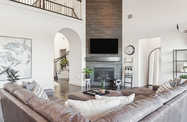 living room featuring a tiled fireplace, dark wood-type flooring, and a high ceiling