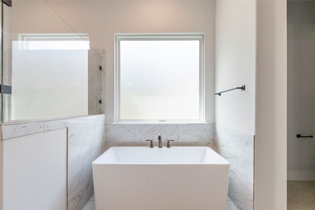 bathroom with a freestanding tub, tile walls, and a wealth of natural light