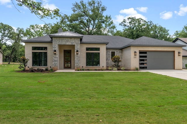 prairie-style home featuring a garage, a chimney, concrete driveway, a front yard, and brick siding