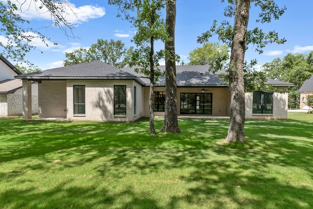 rear view of house featuring a shingled roof, a ceiling fan, brick siding, and a yard