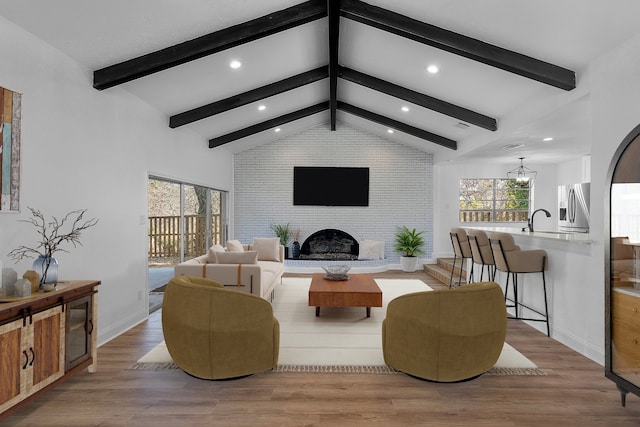 living room featuring a fireplace, light hardwood / wood-style floors, beamed ceiling, and a wealth of natural light