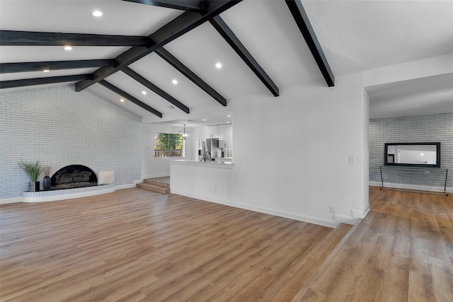 unfurnished living room with brick wall, light hardwood / wood-style flooring, a fireplace, and lofted ceiling with beams