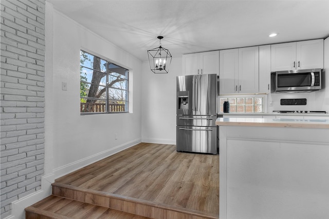 kitchen with decorative light fixtures, white cabinets, appliances with stainless steel finishes, and light hardwood / wood-style floors