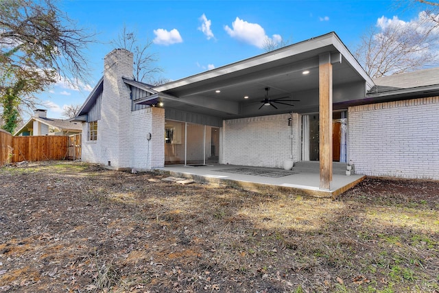 rear view of property with a patio, brick siding, fence, a ceiling fan, and a chimney