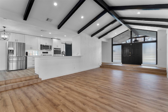 unfurnished living room with light wood-type flooring, beam ceiling, a wealth of natural light, and a barn door