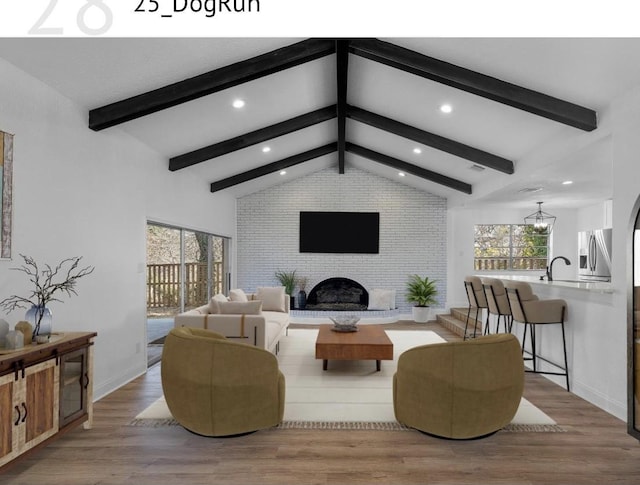 living room with light wood-type flooring, a brick fireplace, vaulted ceiling with beams, and a notable chandelier