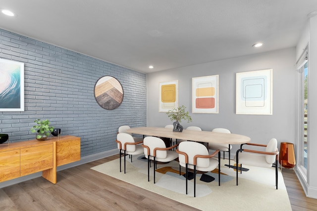dining area featuring brick wall, wood finished floors, recessed lighting, baseboards, and an accent wall