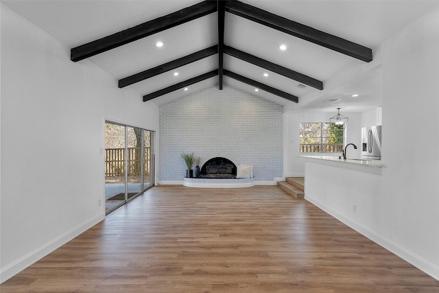 unfurnished living room with a fireplace, light wood-type flooring, beamed ceiling, and sink