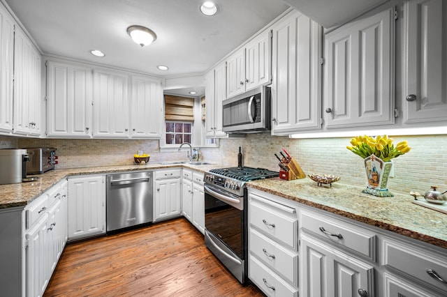 kitchen with appliances with stainless steel finishes, tasteful backsplash, white cabinets, light hardwood / wood-style flooring, and light stone counters