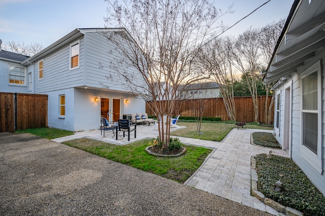 back house at dusk featuring a lawn, an outdoor hangout area, and a patio area