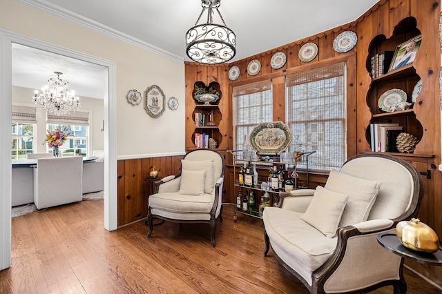 sitting room featuring crown molding, light wood-type flooring, a notable chandelier, and wooden walls