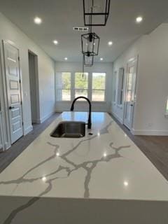 kitchen featuring light stone countertops, decorative light fixtures, a center island with sink, and sink