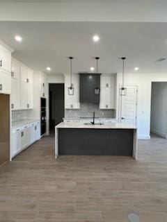 kitchen with decorative light fixtures, white cabinets, tasteful backsplash, and a center island with sink