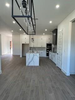 kitchen with a center island, white cabinetry, dark wood-type flooring, double oven, and light stone counters