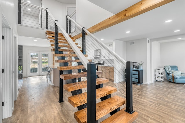 stairway featuring french doors, a towering ceiling, wood-type flooring, and beam ceiling