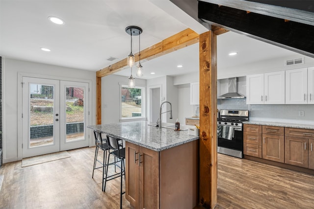 kitchen featuring white cabinetry, sink, light stone counters, stainless steel range with gas stovetop, and wall chimney exhaust hood