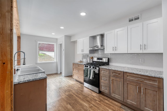 kitchen with white cabinets, stainless steel range with gas cooktop, sink, and wall chimney range hood