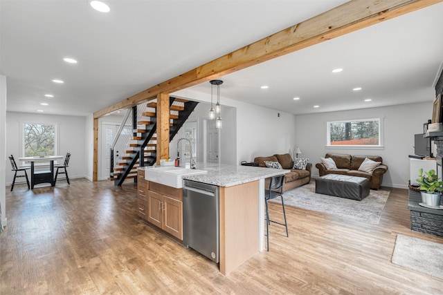 kitchen with pendant lighting, dishwasher, an island with sink, sink, and light hardwood / wood-style floors