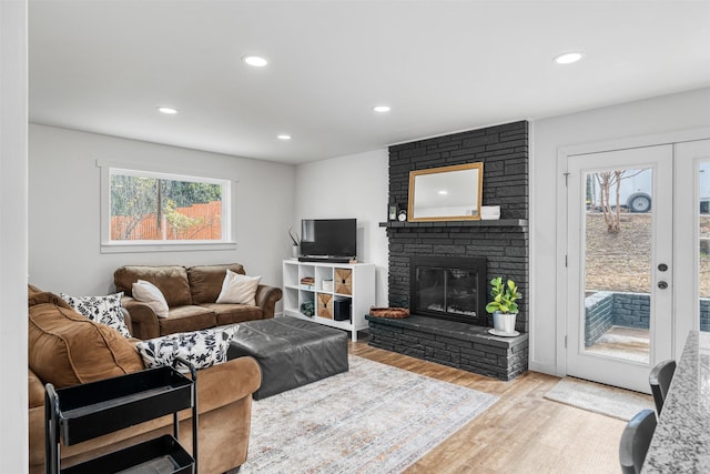 living room with a stone fireplace, light hardwood / wood-style floors, and french doors