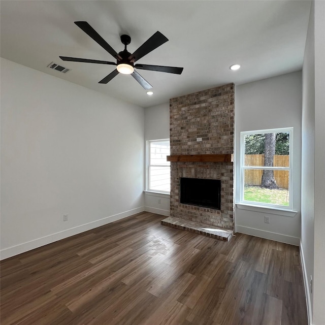 unfurnished living room with a brick fireplace, dark wood-type flooring, ceiling fan, and a healthy amount of sunlight