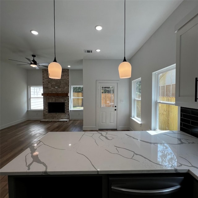 kitchen featuring ceiling fan, dark hardwood / wood-style floors, a fireplace, pendant lighting, and light stone counters