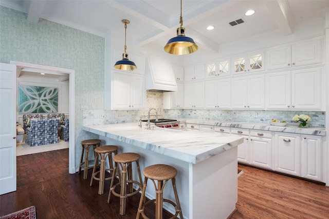 kitchen featuring premium range hood, white cabinetry, hanging light fixtures, beam ceiling, and light stone counters