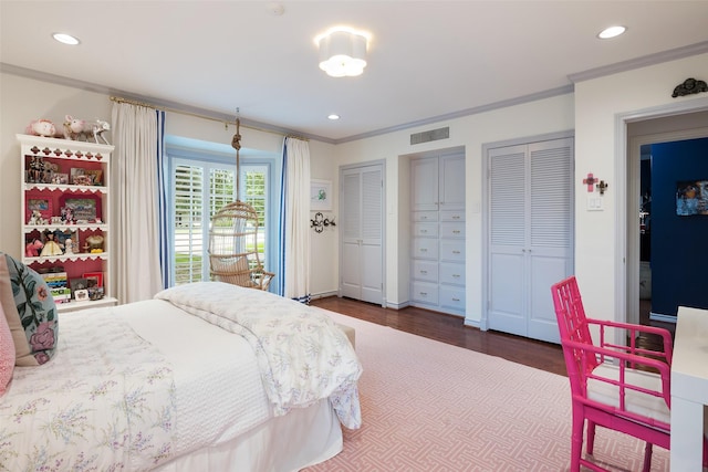 bedroom with dark wood-type flooring, crown molding, and multiple closets