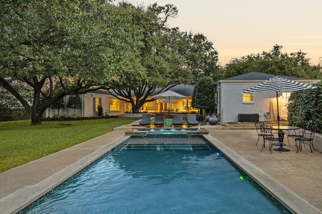 pool at dusk with a patio area, a yard, and an in ground hot tub