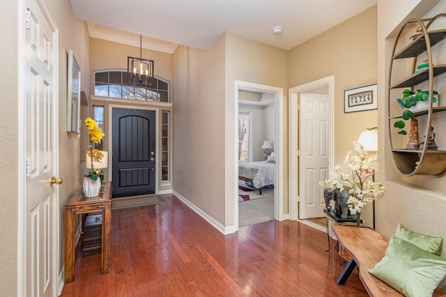 foyer entrance with dark wood-type flooring, a notable chandelier, and crown molding