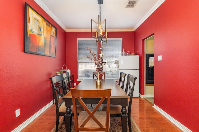 dining room with hardwood / wood-style flooring, ornamental molding, and a notable chandelier