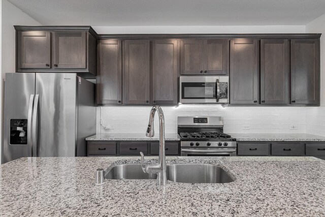 kitchen featuring appliances with stainless steel finishes, sink, decorative backsplash, dark brown cabinetry, and light stone countertops