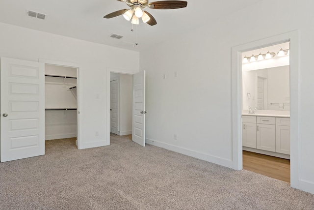 unfurnished bedroom featuring ceiling fan, light colored carpet, ensuite bathroom, a walk in closet, and a closet