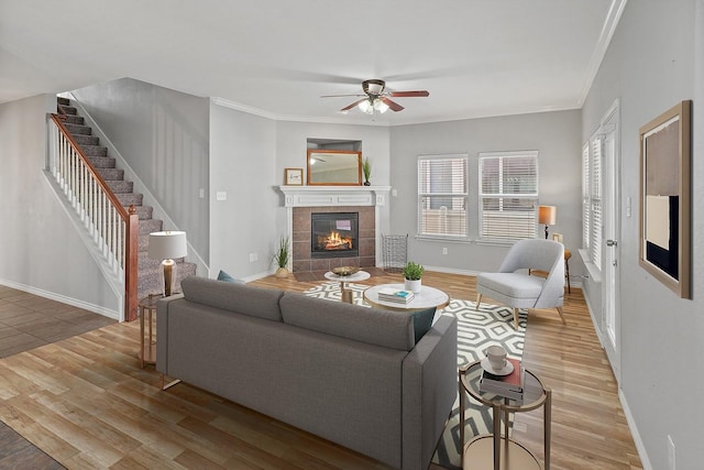 living room with ceiling fan, light wood-type flooring, a fireplace, and ornamental molding