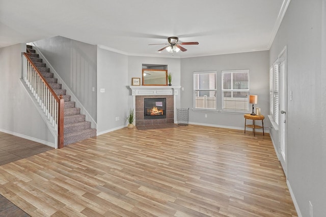 unfurnished living room with ceiling fan, light hardwood / wood-style floors, a tile fireplace, and crown molding