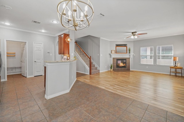 unfurnished living room with crown molding, light wood-type flooring, a tile fireplace, and ceiling fan with notable chandelier