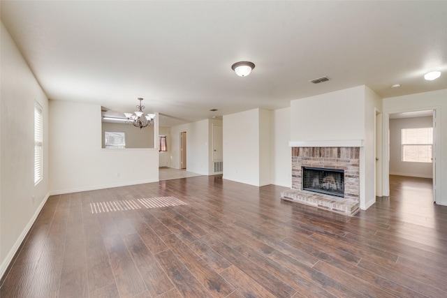 unfurnished living room featuring a healthy amount of sunlight, a fireplace, a chandelier, and dark hardwood / wood-style floors